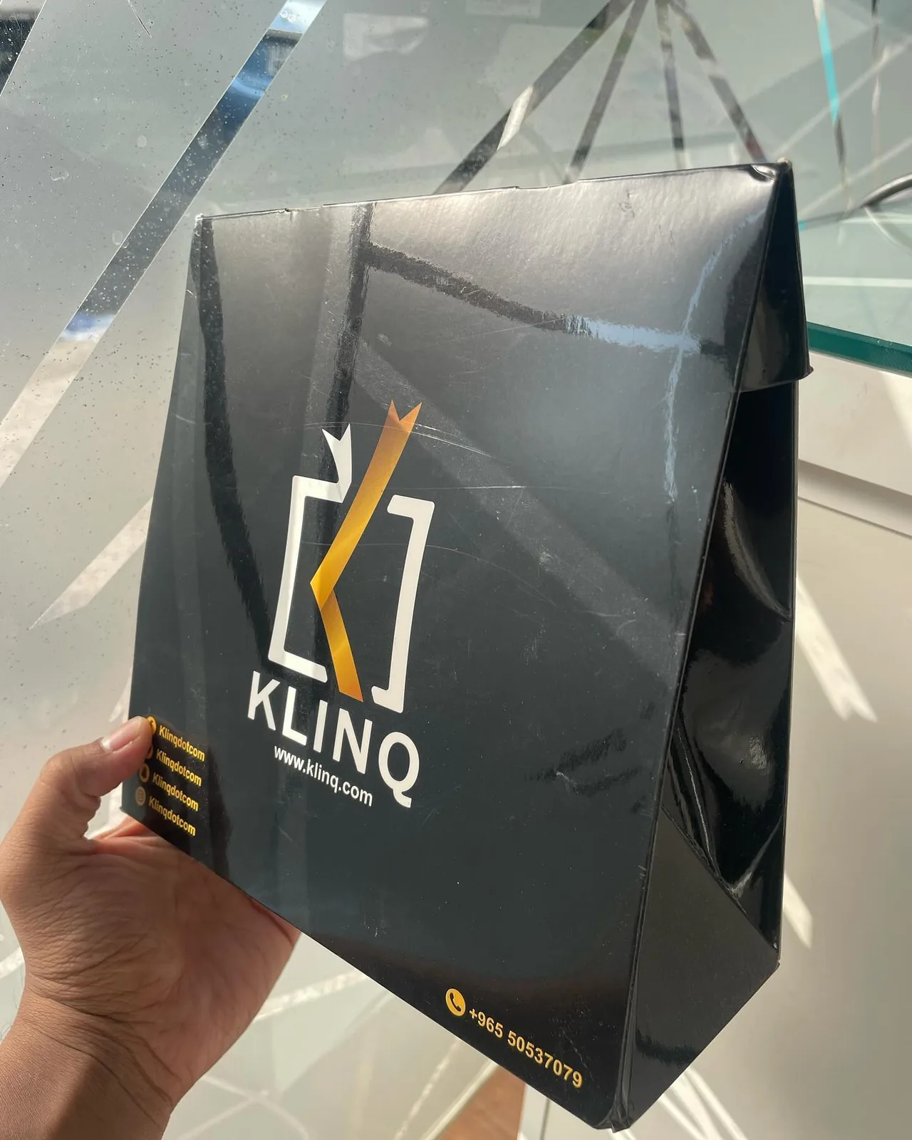Black matte paper bag with gold logo held in hand